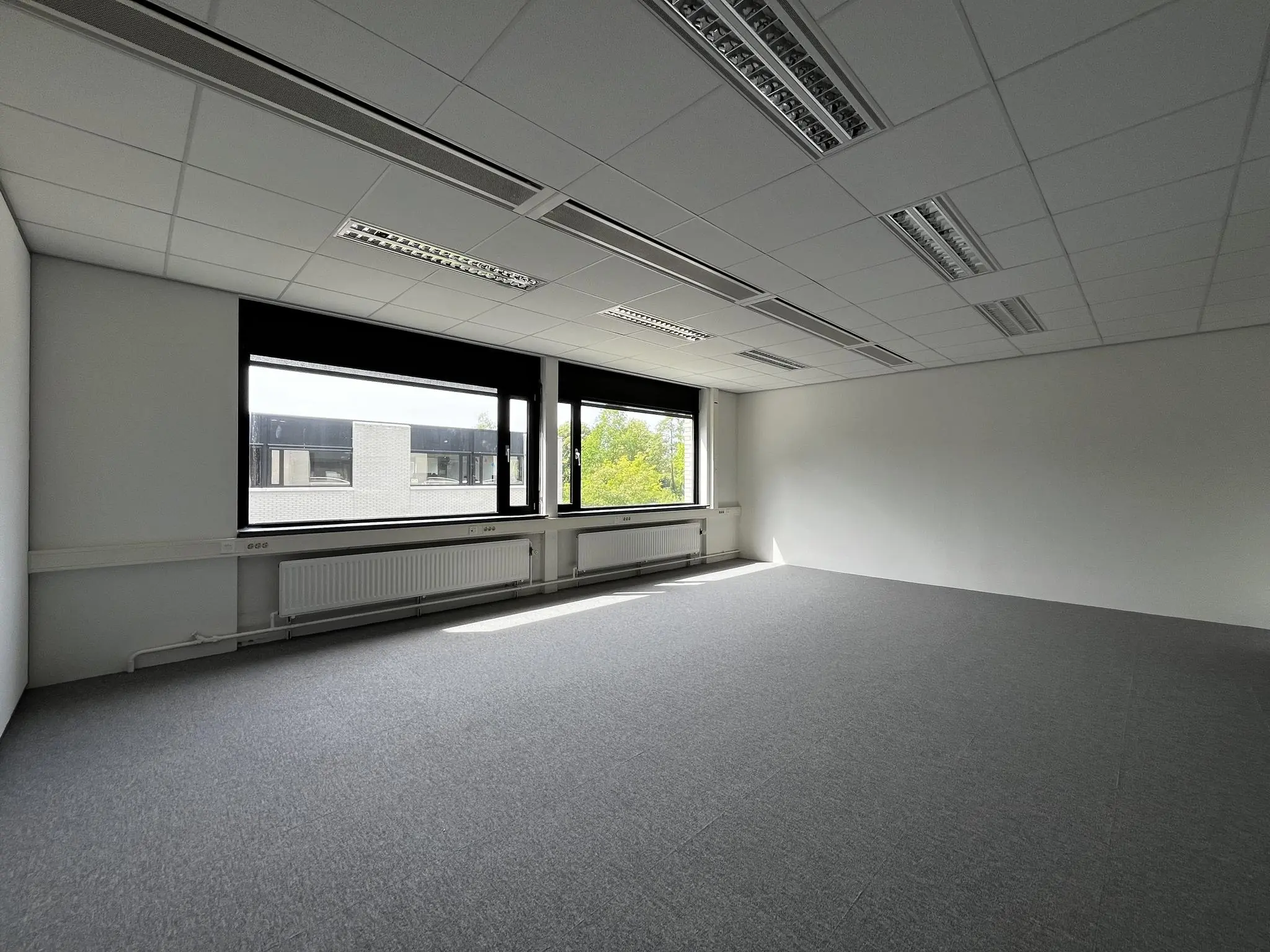 Leeg, licht kantoor met grijs tapijt en grote ramen aan de Burgemeester Verderlaan.